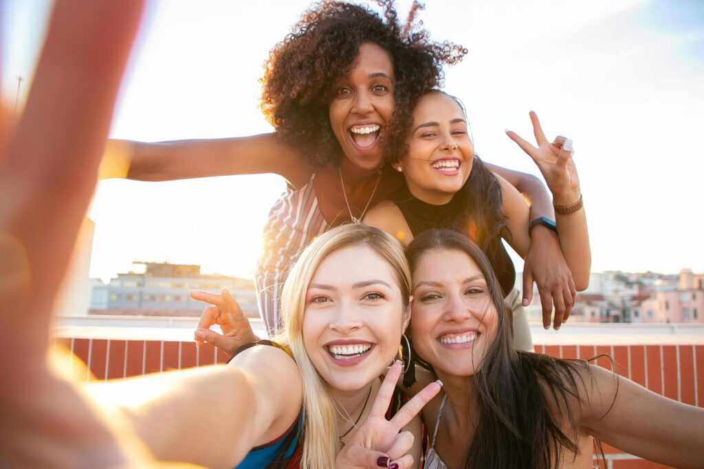 Cheerful friends capturing a fun selfie on a rooftop during sunset, enjoying a positive and trendy moment.